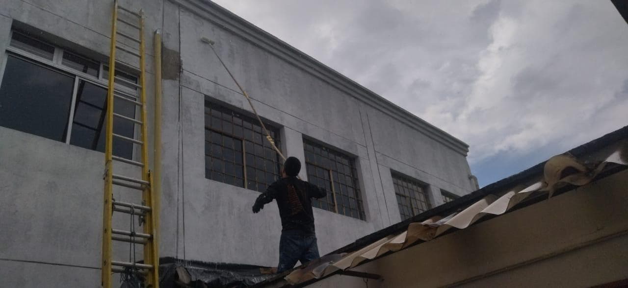 Limpieza de fachada industrial — operario pintando con extensión desde la cubierta